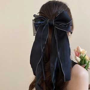 Detail of a large black lace bow hair clip with white trim and elegant long ribbons