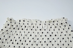 Close-up of black polka dot pattern on smocked elastic fabric with ruffled trim