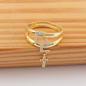 Detail of adjustable gold ring with F-shaped letters, cross charm and zircon stones