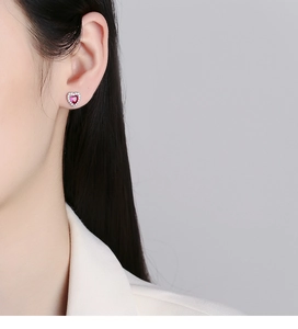 Close-up of heart-shaped earring with red gemstone and white zircon on ear