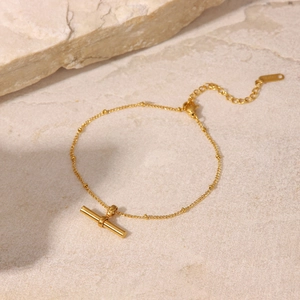 Macro detail of 18K gold titanium steel anklet with T-bar pendant on stone background