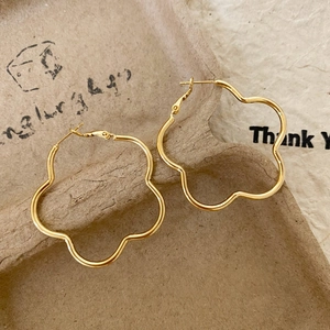 Detail view of gold flower-shaped large earrings on a rustic textured brown backdrop