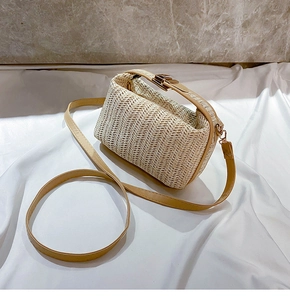 Close-up of beige woven straw shoulder bag with PU strap on white fabric surface