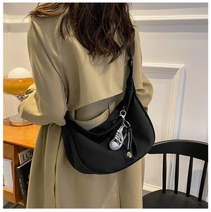 Side view of a large black canvas crossbody dumpling bag worn by a model in a cozy room