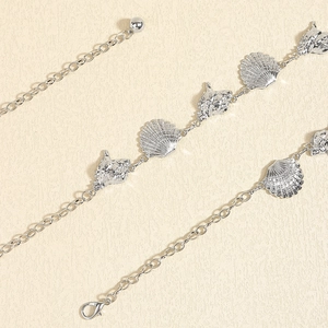Detailed silver body chain featuring starfish and seashell charms on textured beige background