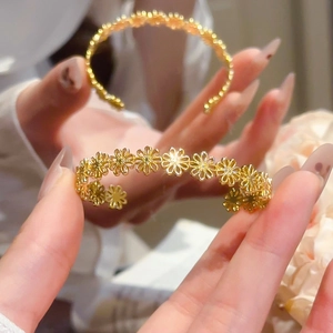 Detailed close-up of golden hollow daisy flower patterns on elegant open cuff bracelet