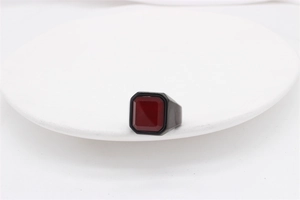 Close-up of a men's matte black steel ring with a large square red gemstone inlay