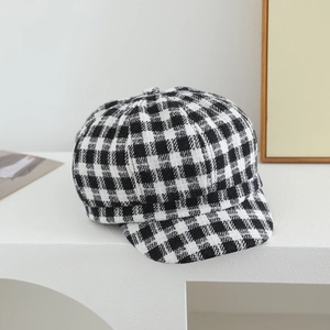 Detailed texture of a classic black and white plaid newsboy cap on a white display stand