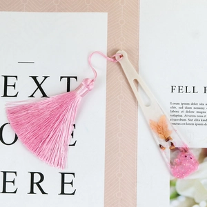 Détail d'un marque-page artisanal en résine avec fleurs séchées et pompon rose long