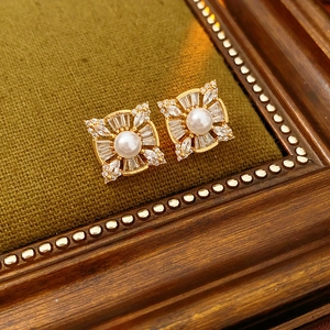 Detailed view of gold pearl stud earrings with zircon floral pattern on green fabric