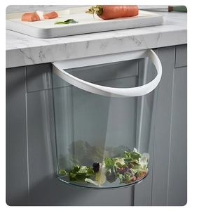 Transparent wall-mounted kitchen waste bin hanging on a grey cabinet door