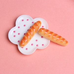Détail de deux baguettes miniatures en résine sur une assiette à pois pour maison de poupée