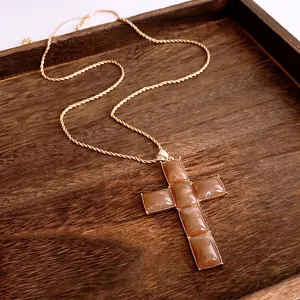 Retro resin cross pendant with golden twist chain on dark wood tray