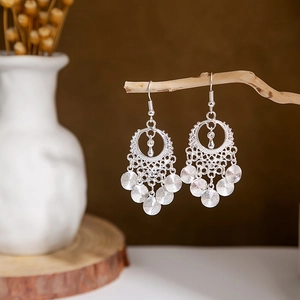 Detailed close-up of bohemian silver earrings with leaf hollow patterns and round tassels