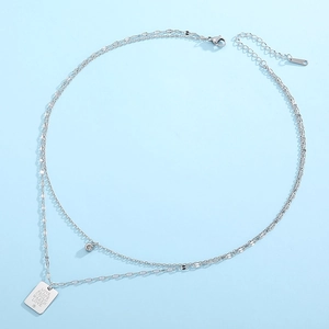 Macro shot of double-layered silver necklace with engraved rectangle pendant detail