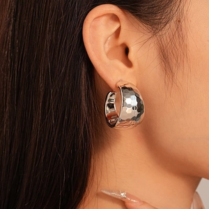 Close-up of a wide silver C-shaped metal hoop earring with hammered texture on model