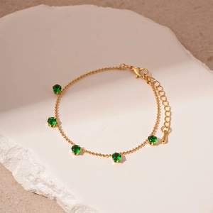 Close-up of a gold beaded bracelet featuring five vibrant green round zircon gemstones