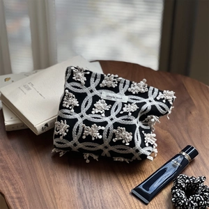 Close-up of butterfly embroidery and pom-pom trim on a linen cosmetic pouch
