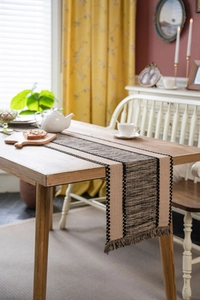 Close-up of woven table runner with black stripe patterns and decorative tassels