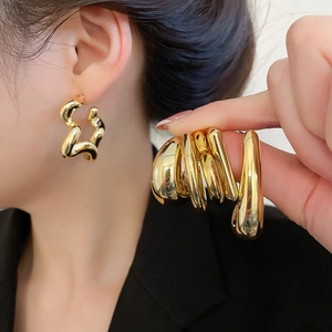 Macro detail of large irregular gold geometric earrings with a high-polished glossy finish