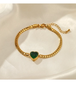 Close-up of golden heart bracelet with green gemstone on elegant white silk
