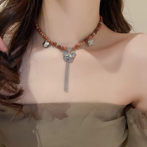 Gros plan du collier en perles de santal rétro avec pendentifs papillons et glands à chaîne