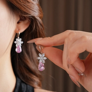 Gros plan sur les boucles d'oreilles fleurs avec gouttes roses tenues à la main
