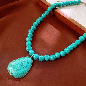Close-up of vintage beaded necklace with turquoise water-drop pendant on dark leather