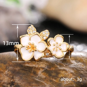 Golden ring with two white enamel flowers and clear diamonds on stone background