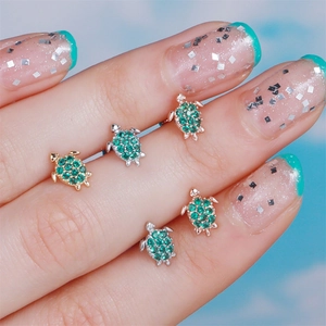 Macro view of turtle piercing studs with emerald green cubic zirconia in gold and silver