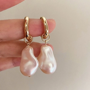 Close-up of golden hoop earrings featuring natural Baroque pearls with soft pink luster
