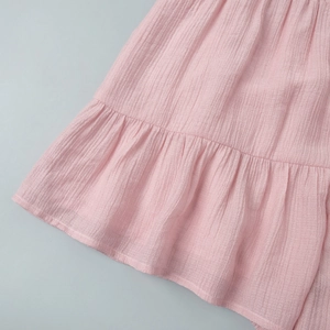 Detailed close-up of pink crepe fabric featuring textured ruffles and pleated hemline