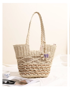Detail of hollow straw shoulder bag featuring a woven flower and purple butterfly accent