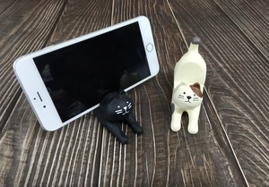 Cat-shaped resin phone holder supporting a smartphone on a dark wood background