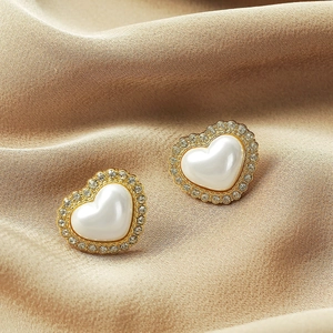 Macro detail of heart-shaped gold stud earrings with crystal halo and pearl center