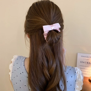 Detail of pink satin bow scrunchie on dark brown hair showing soft silk texture