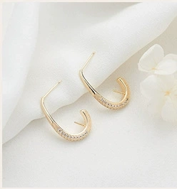 Macro shot of gold U-shaped earrings set with sparkling cubic zirconia on white fabric