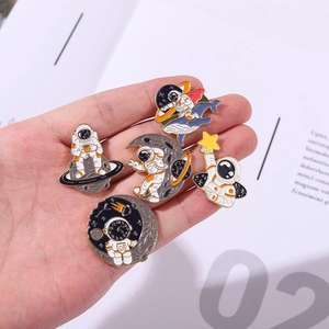 Astronaut and whale enamel pins held in hand featuring moon and planet space themes