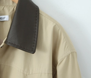 Detail of khaki trench coat featuring a brown leather collar with decorative stitching