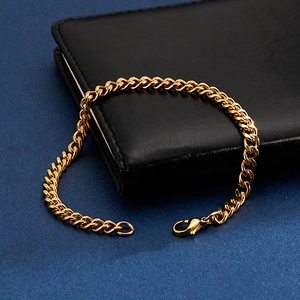 Polished gold cuban link chain bracelet with lobster clasp on a dark leather notebook