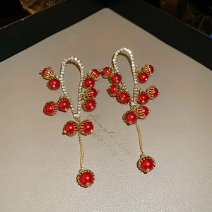 Dettaglio di orecchini pendenti a fiore rosso con finitura dorata e zirconi lucidi