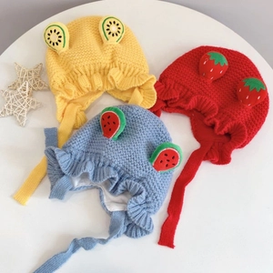 Three knitted baby earflap hats in yellow, red, and blue with cute fruit decorations