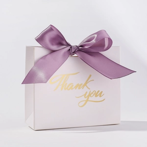 Detail of white wedding favor box with a purple satin bow and gold Thank You text