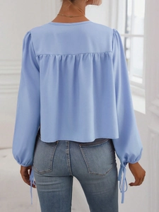 Vista trasera de blusa azul claro con mangas abullonadas y lazo de ajuste holgado