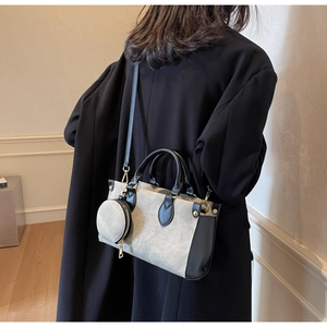 Detail of gray textured crossbody bag with gold hardware shown on a model's coat