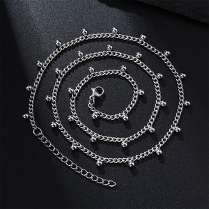 Minimalist stainless steel necklace featuring small foot pendant and beads on black texture