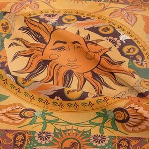 Macro texture of Bohemian tapestry showing sun motif and astrological zodiac symbols