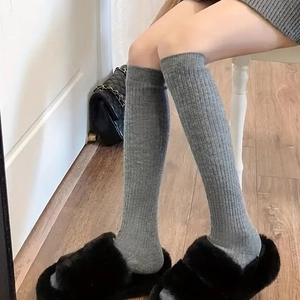Close-up of grey ribbed knitted over-the-knee socks for women in cozy home interior