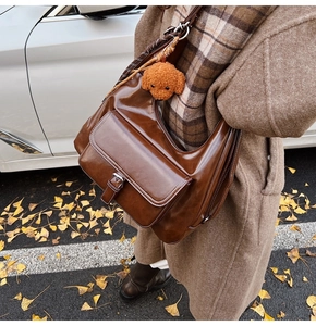 Detail of dark brown glossy leather shoulder bag with buckle pocket and plush puppy charm