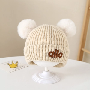Detail von beiger Strickmütze für Kleinkinder mit zwei Bommeln und Stickerei